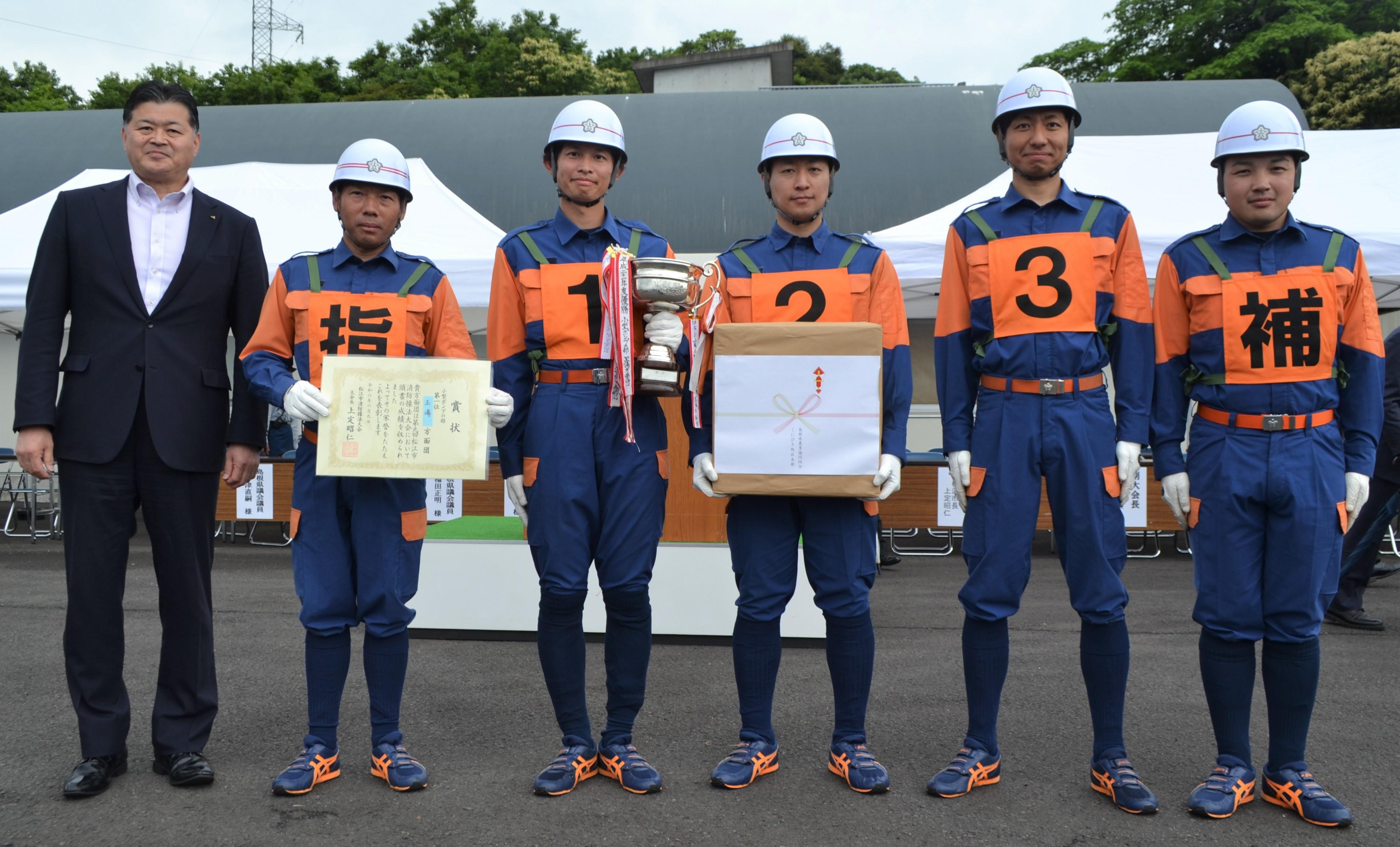 優勝した玉湯方面団の団員と越野本部長(左).jpg